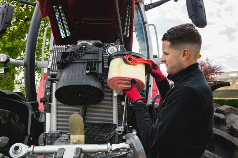 Henkilö huoltamassa Massey Ferguson -traktoria ja vaihtaa siihen suodatinta