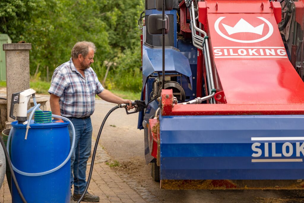 Mies tankkaa polttoainetta letkulla seosrehuvaunuun.