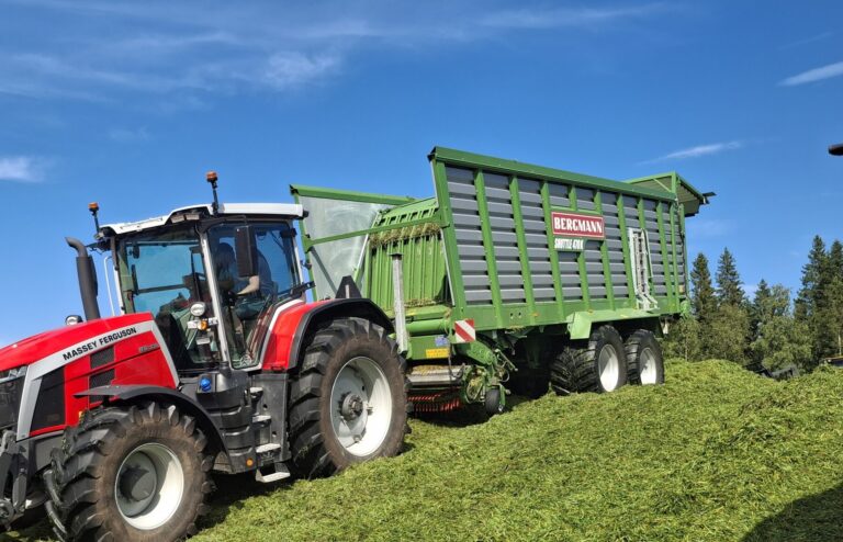 Massey Ferguson -traktori ja Bergmann Shuttle -noukinvaunu rehuaumassa purkamassa rehukuormaa.