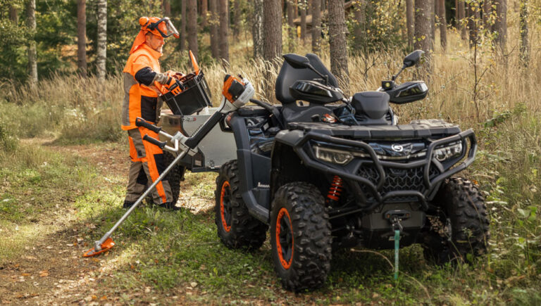 CFMOTO -mönkijät, Stihl-raivaussaha ja mies metsurin vaatteissa metsätiellä.