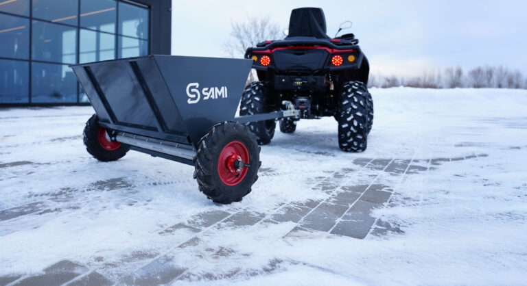 Sami S-290 hiekoitin mönkijän perässä rakennuksen edessä.