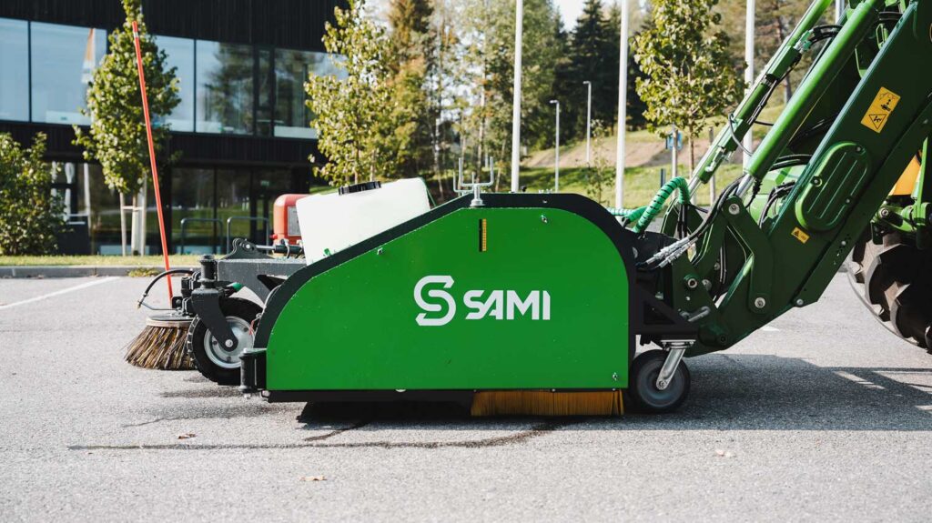 Sami keräävä harjakone lakaisee parkkialuetta, kuva sivusta.