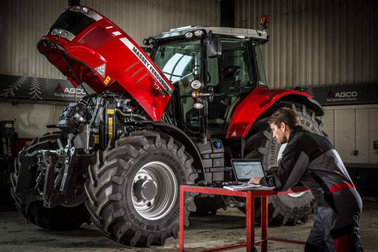 Massey Ferguson -traktori huollossa ja huoltohenkilö tutkii varaosakirjoja tietokoneelta.