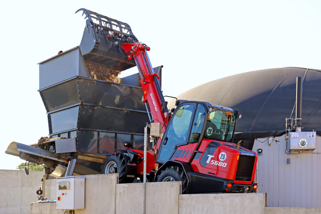 Schäffer 5680 T-3 -teleskooppikuormaaja nostamassa materiaalia kärryille.