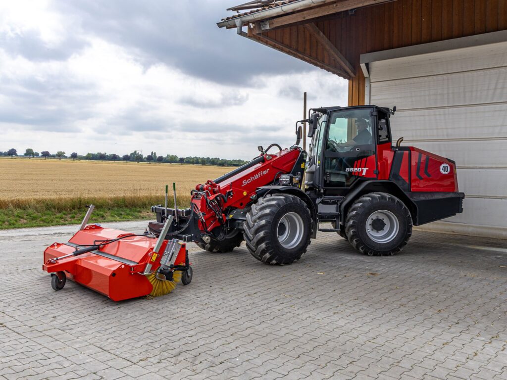 Schäffer 8620 T-3 -teleskooppikuormaaja lakaisemassa pihaa.