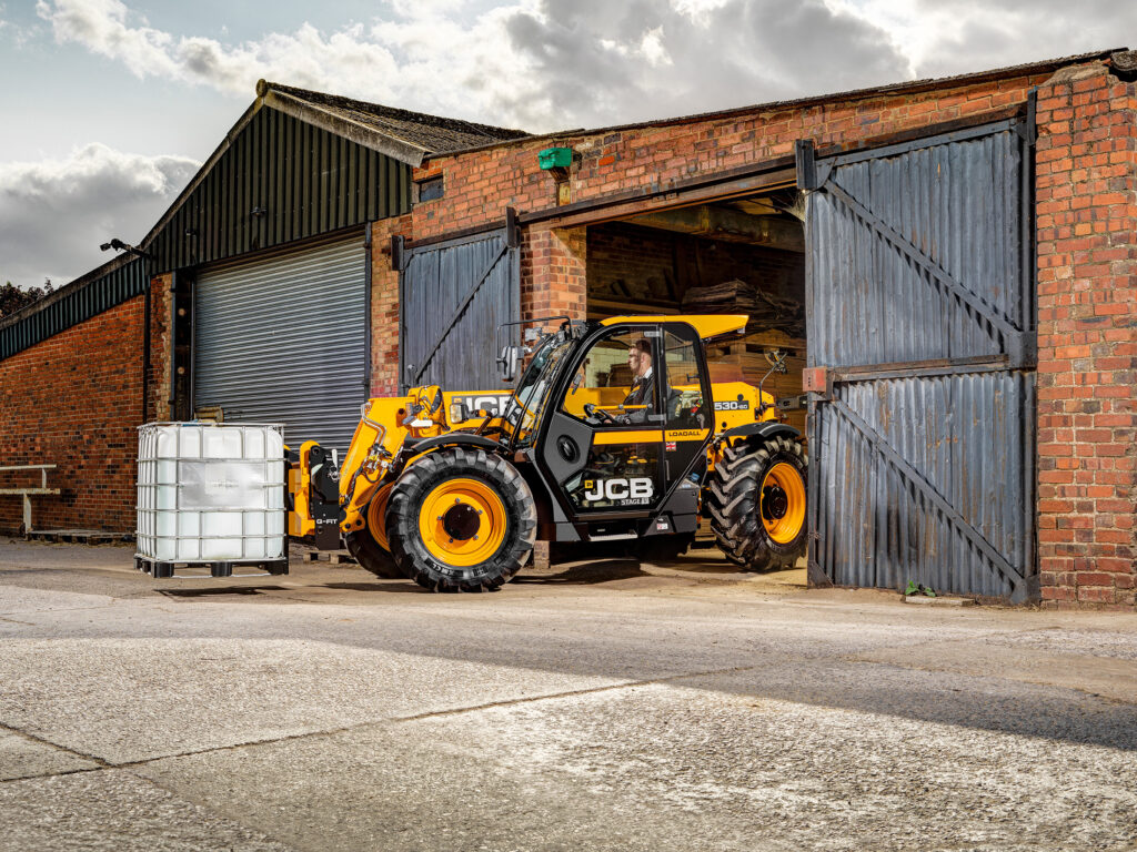 JCB 530-60 Agrisuper -kurottaja tulossa vanhasta maatilarakennuksesta.