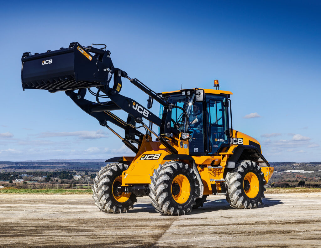 JCB 413S-pyöräkuormaaja maatilan pihalla ajamassa.