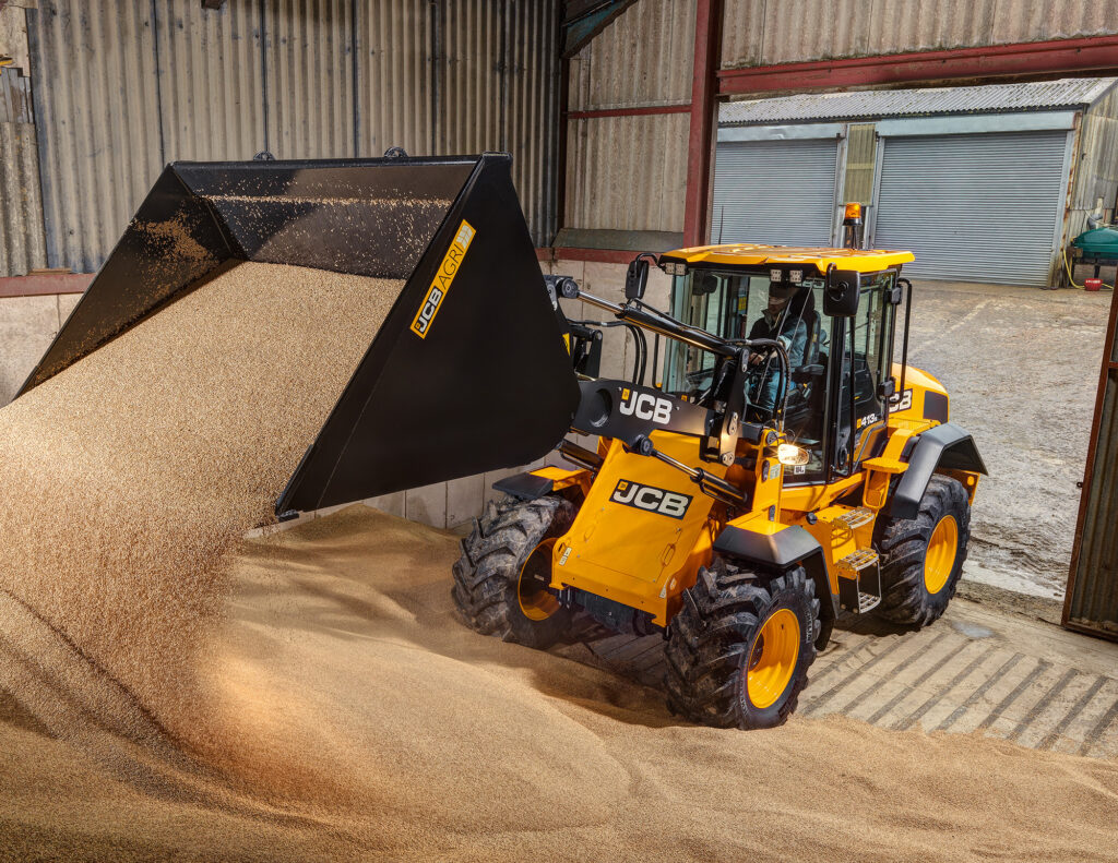 JCB 413S-pyöräkuormaaja kaatamassa viljaa säilöön maatilalla.