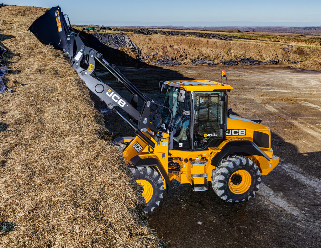 JCB 413S-pyöräkuormaaja nostamassa rehua aumasta.