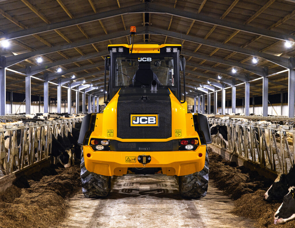 JCB 413S-pyöräkuormaaja siirtämässä rehua ruokintapöydällä navetassa.