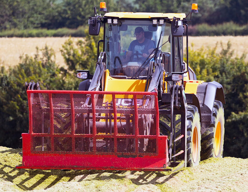 JCB 419S-pyöräkuormaaja rehua aumalla työskentelemässä.