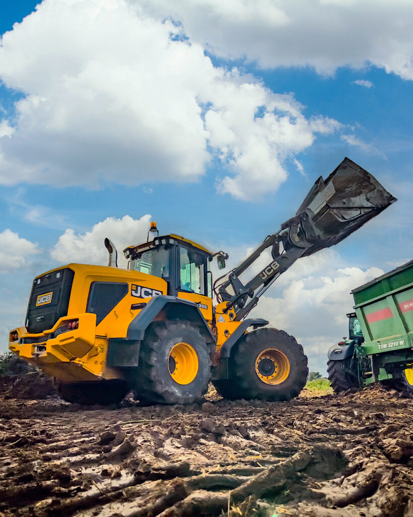 JCB 435S -pyöräkuormaaja nostamassa lantaa Bergmann-lannanlevittimeen.
