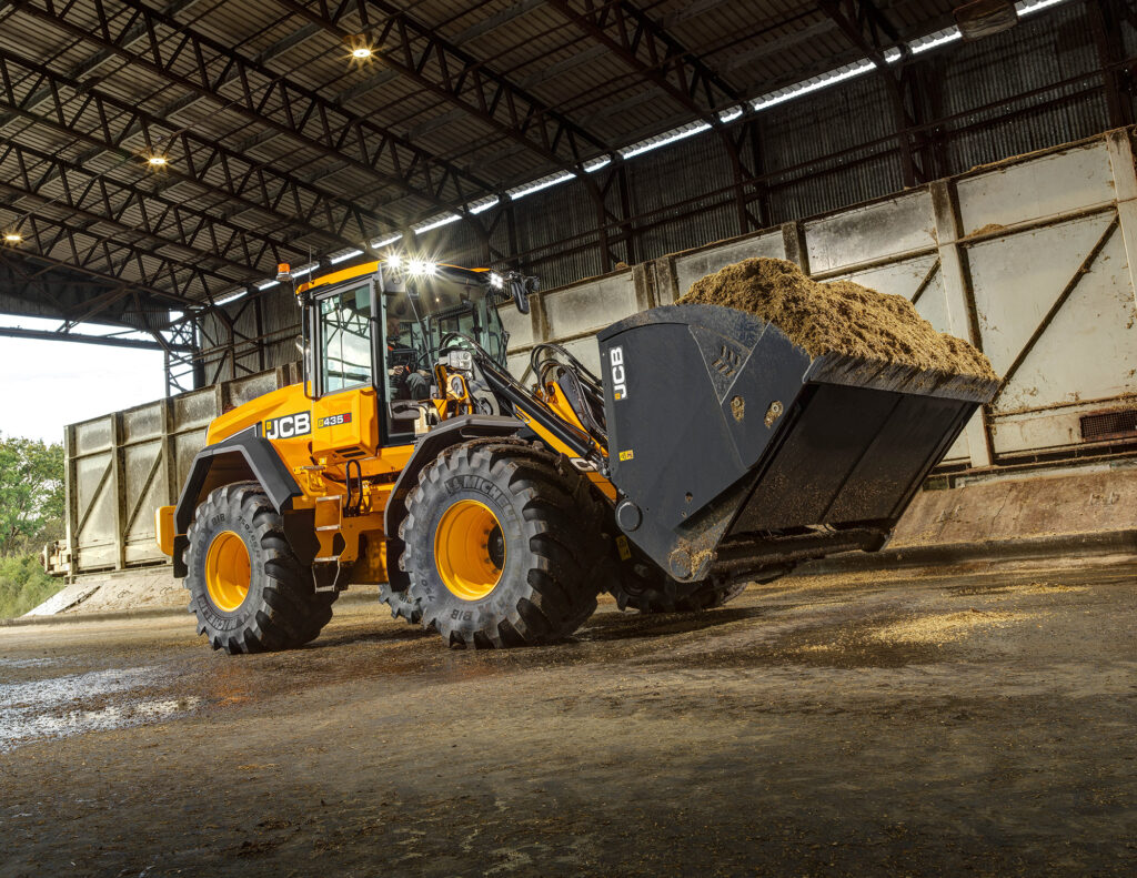 JCB 435S -pyöräkuormaaja maatilalla kantamassa rehua.