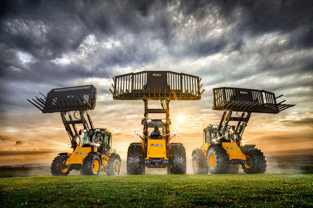 Kolme JCB-pyöräkuormaajaa kauhat ylhäällä.
